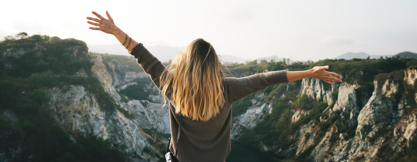 Ženska z razprtimi rokami stoji na robu skalnatega kanjona in gleda v naravo