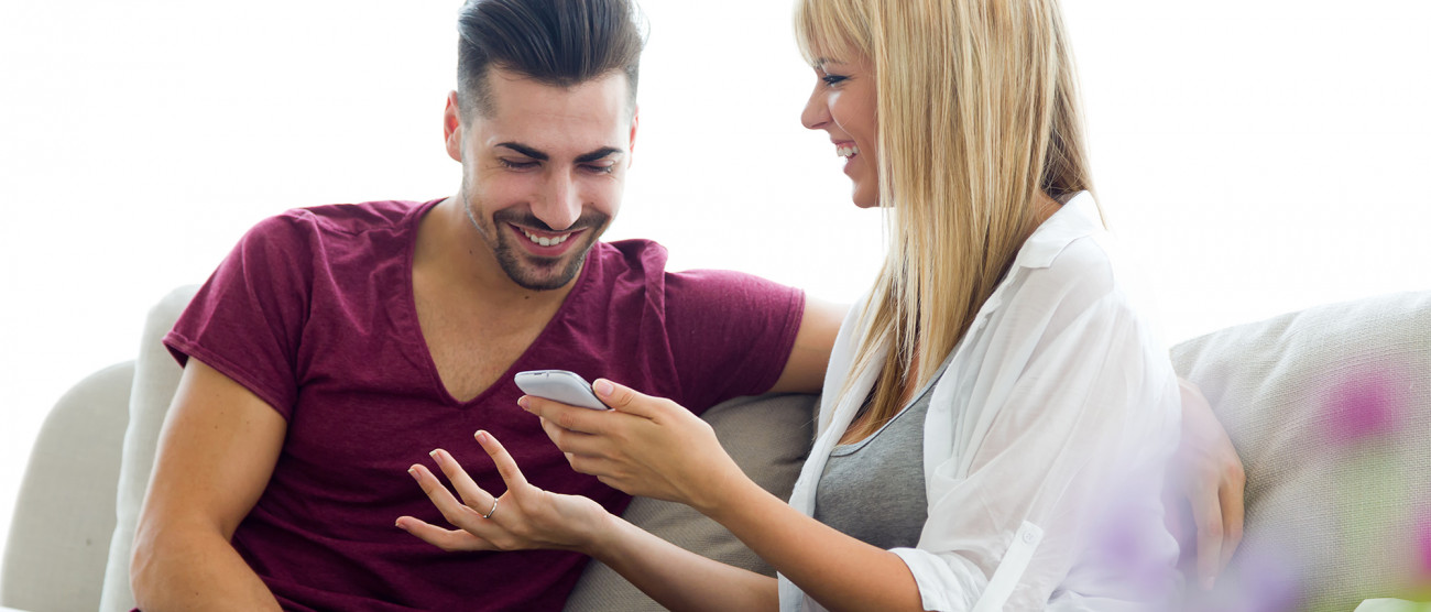 Nasmejan par sedi na kavču in skupaj gleda telefon med sproščenim pogovorom