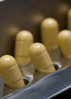 Rumene kapsule so vstavljene v kovinski proizvodni kalup v farmacevtskem obratu