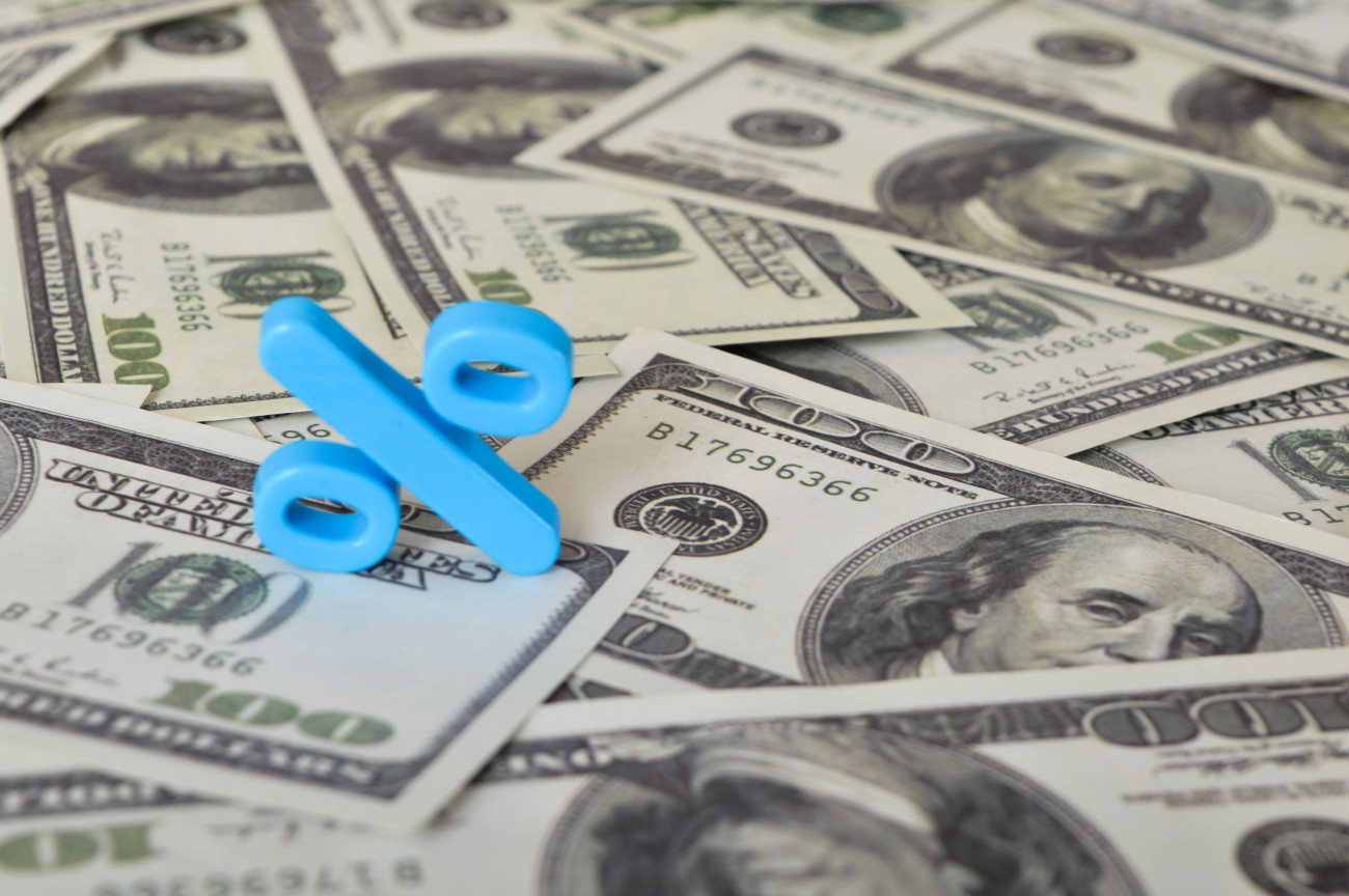 Modri znak za odstotek leži na kupu ameriških stodolarskih bankovcev z Benjaminom Franklinom