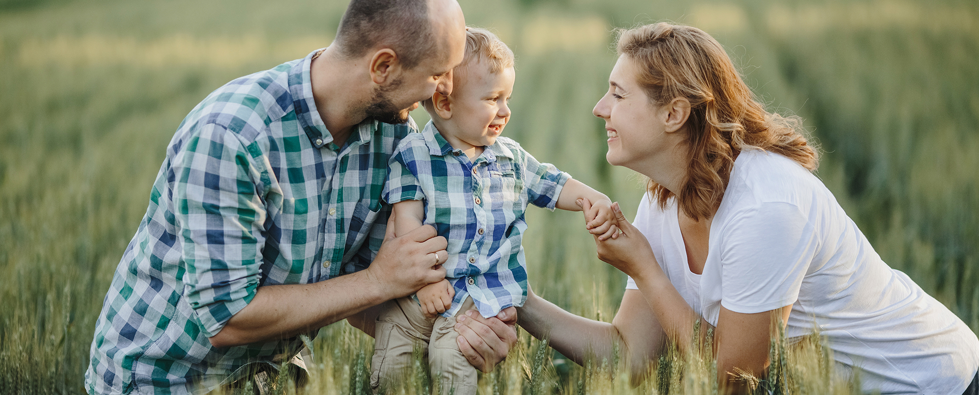 Nasmejana družina s staršema in otrokom se igra na zelenem polju med travo in žitom