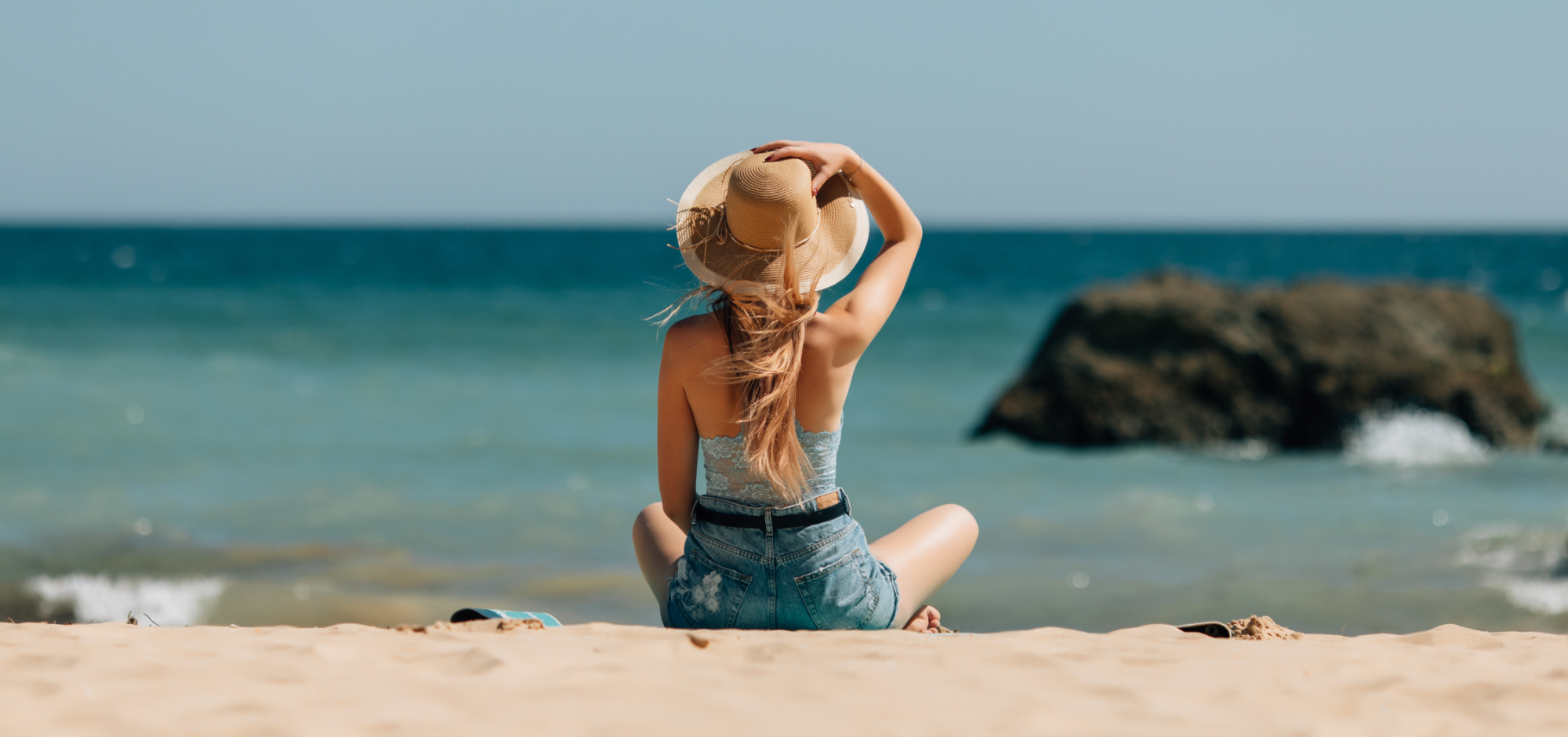 Ženska sedi na peščeni plaži in gleda proti obzorju