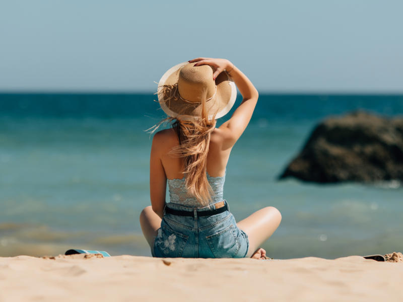 Ženska sedi na peščeni plaži in gleda proti obzorju