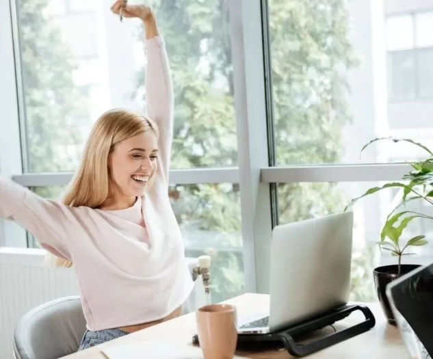 Zadovoljna ženska sedi za pisalno mizo, na kateri je prenosni računalnik