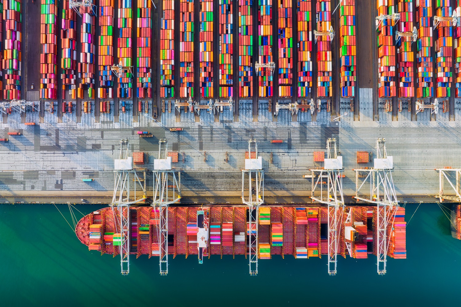 Pogled iz zraka na kontejnersko pristanišče z ladjo, žerjavi in barvnimi zabojniki ob obali