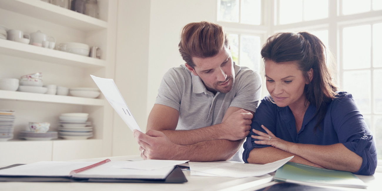 Moški in ženska sedita za kuhinjsko mizo in gledata v finančne dokumente