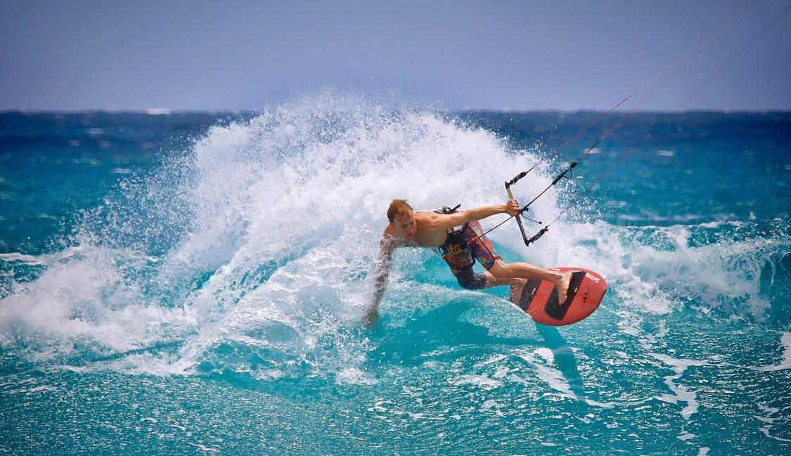 Na sliki je kajtar ki z veliko hitrostjo jadra po valovih turkiznega morja