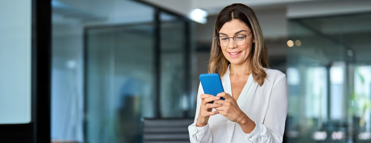 Ženska z očali v pisarni, ki drži modri telefon v roki
