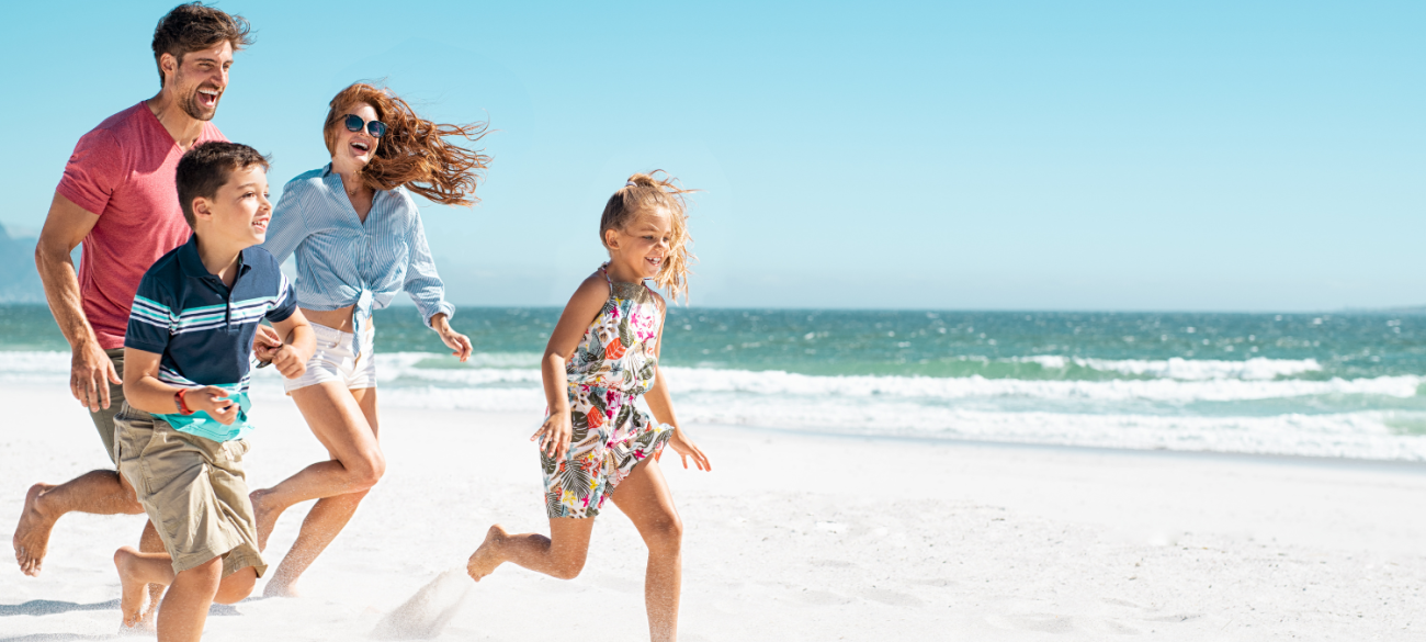 Srečna družina v poletnih oblačilih teče in se smeji na sončni peščeni plaži ob modrem morju