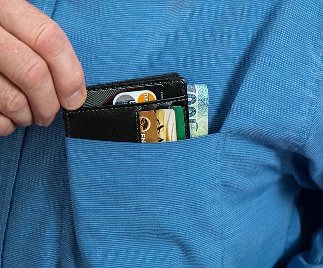 Moški prijema denarnico z denarjem in kreditnimi karticami, ki jo ima v žepu srajce