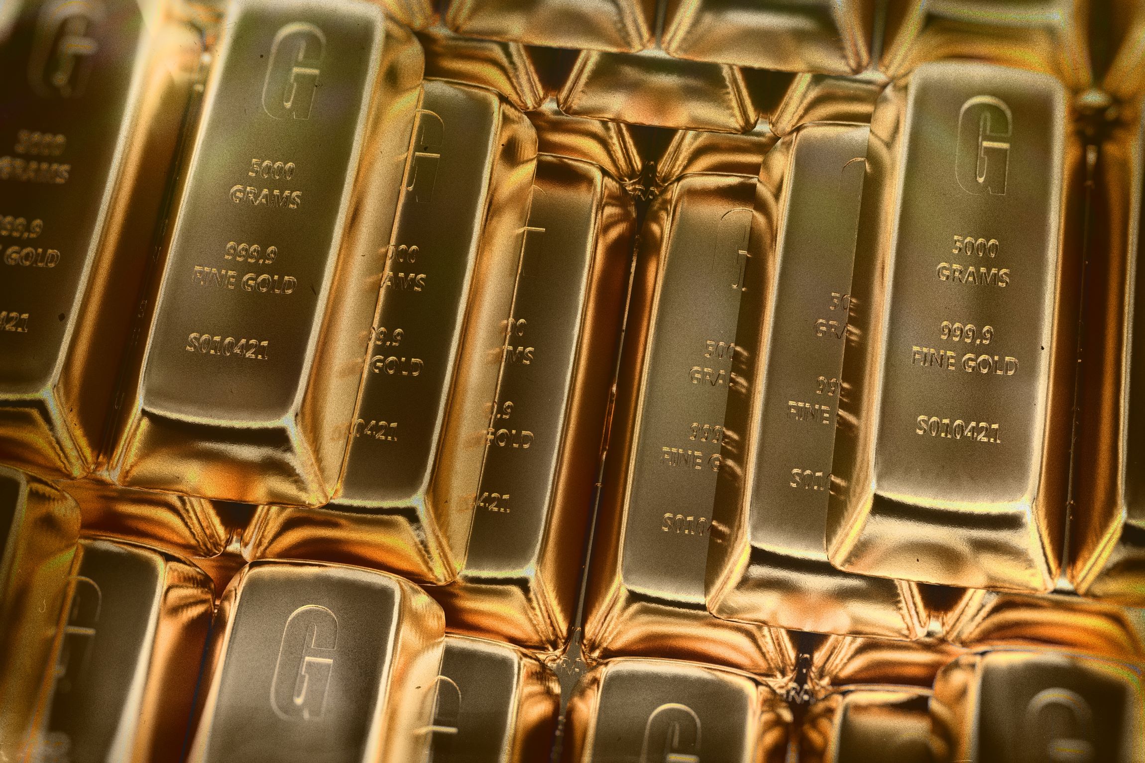 Kup bleščečih zlatih palic z oznako 5000 gramov in čistino 9999 leži zloženih v tesnem vzorcu