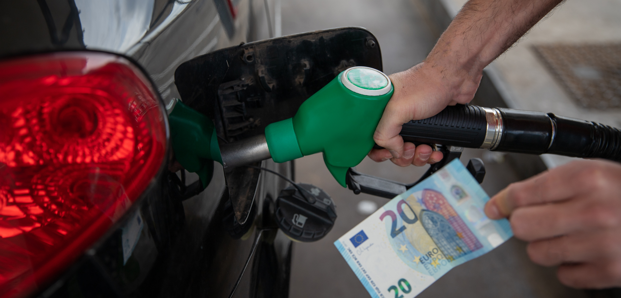 Oseba toči gorivo v avtomobil, v roki drži bankovec za 20 evrov