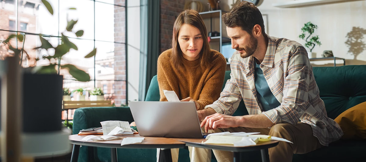 Par v tridesetih sedi na kavču in gleda v prenosni računalnik na klubski mizici