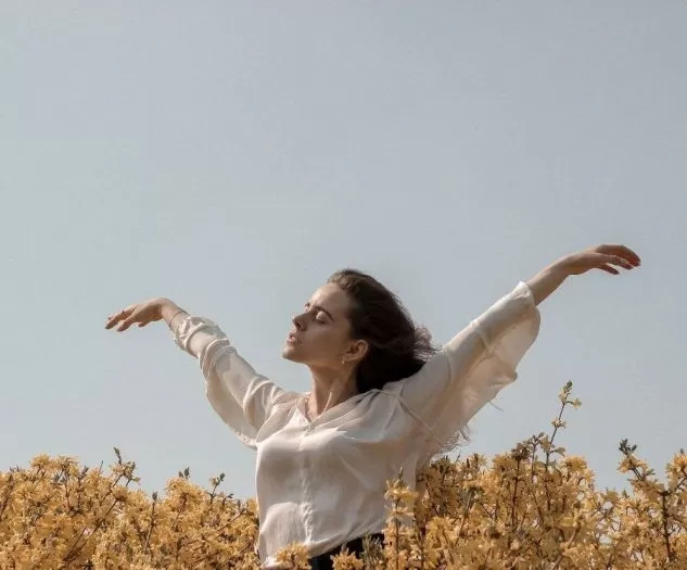 Ženska sredi žitnega polja z razprtimi rokami, ki ponazarjajo svobodo