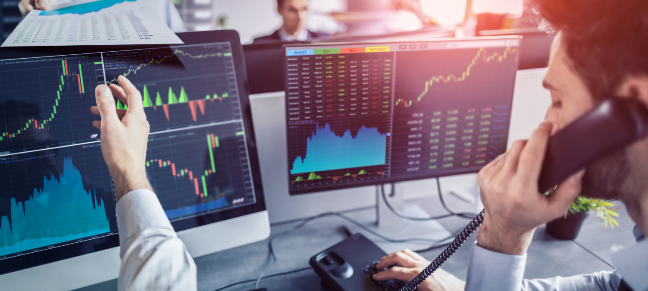 Trgovec na finančnem trgu analizira grafe na dveh zaslonih medtem ko telefonira in drži miško v roki