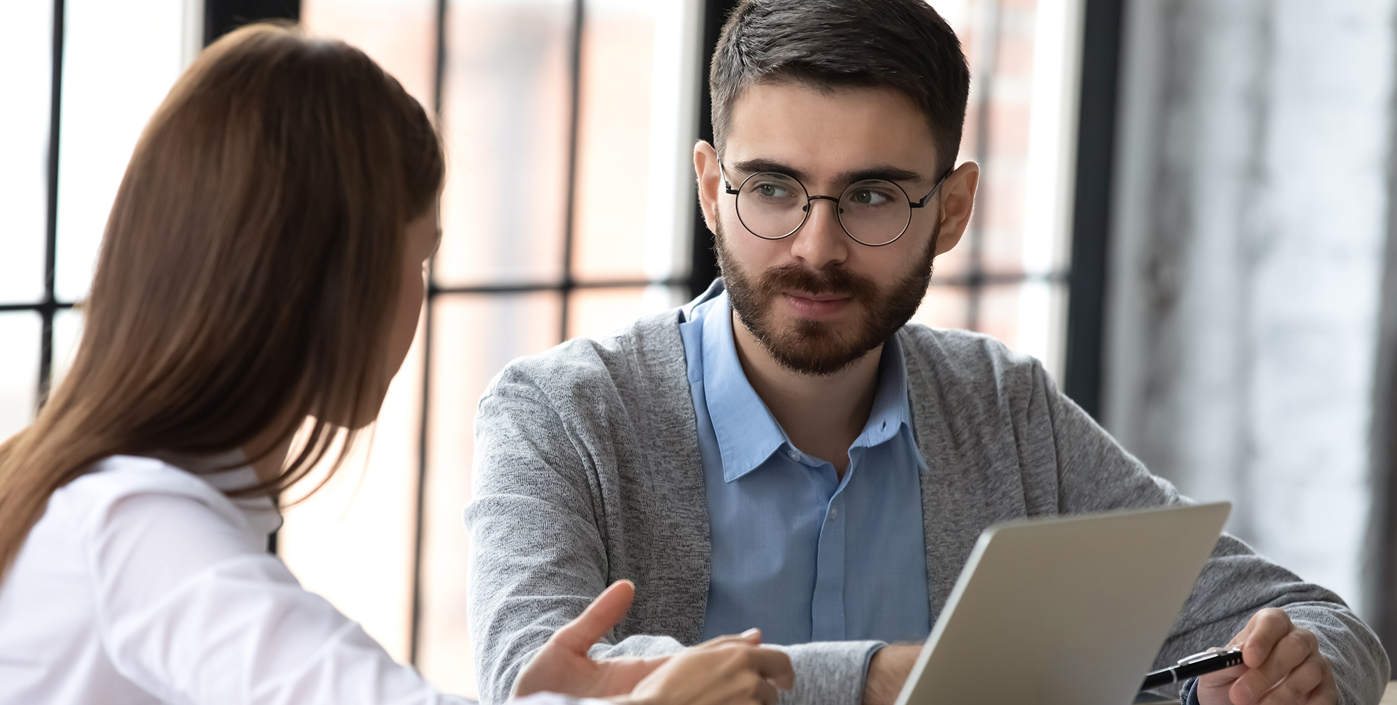 Moški in ženska se pogovarjata za mizo z odprtim prenosnikom medtem ko si zbrano izmenjujeta poglede in informacije