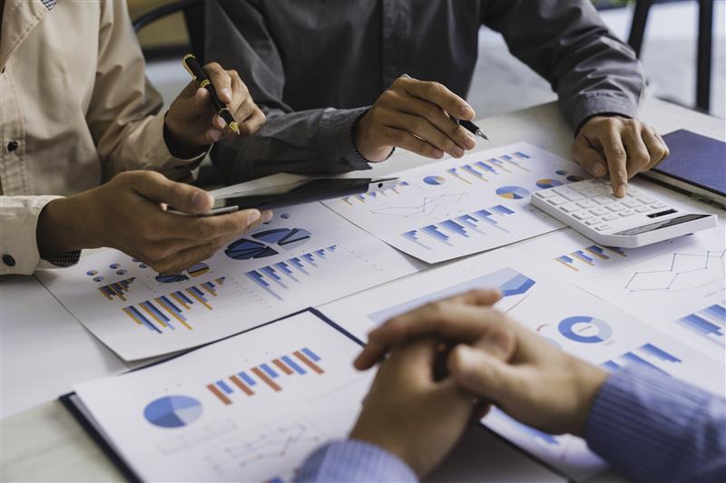 Osebe za mizo pregledujejo finančne grafe in podatke ter uporabljajo kalkulator in telefon