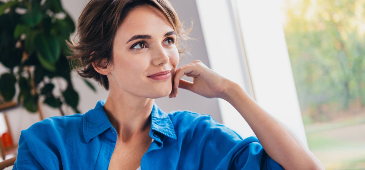 ženska v modri srajci gleda skozi okno