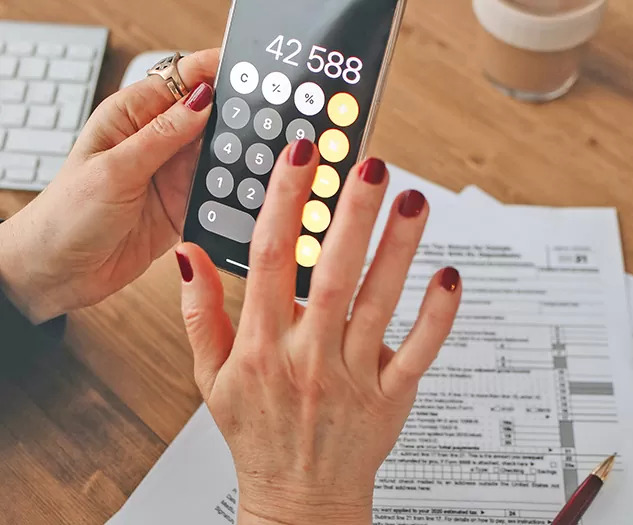 Oseba drži v rokah mobilni telefon z aplikacijo kalkukator ter računa