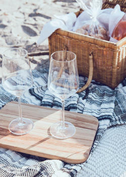 Na piknik odeji na plaži stojita prazna vinska kozarca ob leseni deski poleg košare s hrano steklenico vina in skodelico jagod