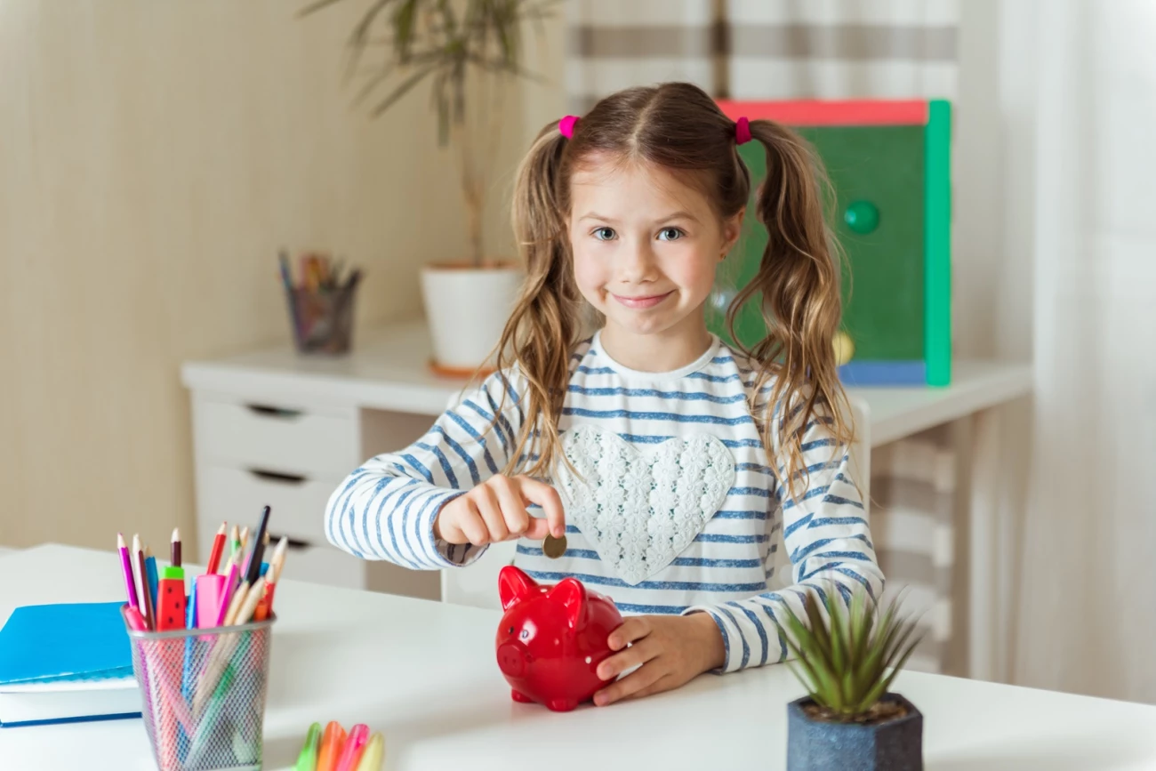 otrok mlada punca za delovno mizo daje kovance v rdeč šparovček